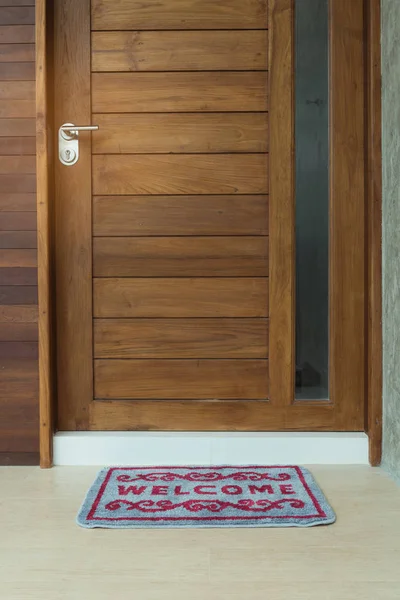 Welcome door mat infront of teak wooden door background