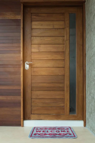 Alfombra de puerta de bienvenida frente al fondo de la puerta de madera de teca — Foto de Stock