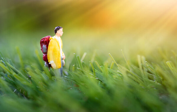 Miniature people, backpack traveler walk in nature green meadow b
