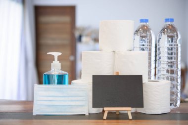 Coronavirus ya da COVID-19 korumaları nedeniyle ev karantinası cerrahi maske, el jeli, doku rulosu, içme suyu şişesi ve oturma odasındaki kara tahta levhası