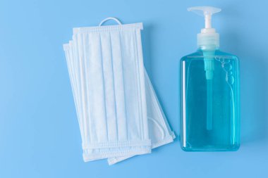 Mikrop koruması ve jel alkolü veya el dezenfektanı şişesi takmak için cerrahi maske. Mavi arka planda kurulmuş Corona sirkinden korumak için, el dezenfektanı şişesi.
