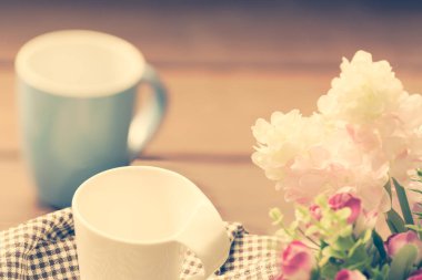 Ahşap masanın üzerinde mavi ve beyaz kahve fincanları çiçek desenli arka plan, retro filtre görüntüsü