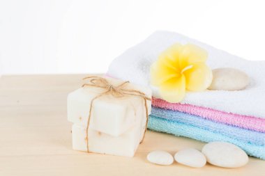 Zen taşı, havlu, hindistan cevizi sabunu ve beyaz arka planda izole edilmiş ahşap masa üzerindeki frangipani çiçekleriyle kaplıca ve tedavi