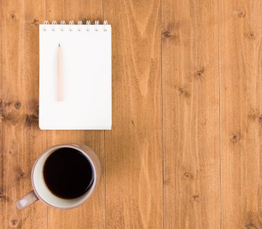 Asgari çalışma alanı, kahve fincanı, defter, tahta masadaki kalem, üst görünüm