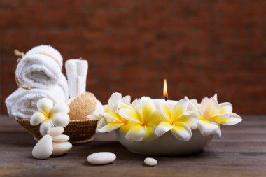 Temel yağlar, zen taşı, havlular, mum, kalp masajı topu ve ahşap duvarlı ahşap masa üzerindeki frangipani çiçekleri ile kaplıca sağlığı ve tedavi