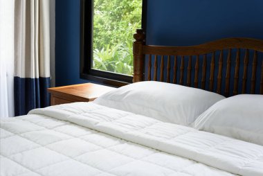 Beyaz yastıklar, yatak çarşafları ve mavi yatak odasındaki ahşap masa.  