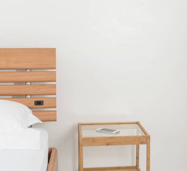 Cep telefonu ahşap sehpada, modern beyaz yatak odasında dekore edilmiş. 