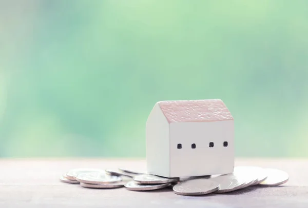 Saving money for house,silver coins and house model on wood table with pastel blurred background