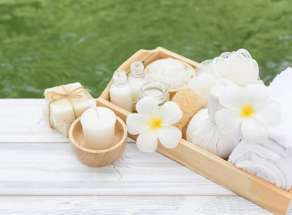 温泉健康概念 白色蜡烛 花和草药按摩球放在绿色池塘背景的白色木桌上 — 图库照片
