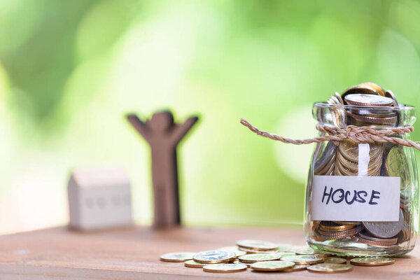 Saving money for house,coins in glass jar with quote house,people model on wood table with pastel blurred background