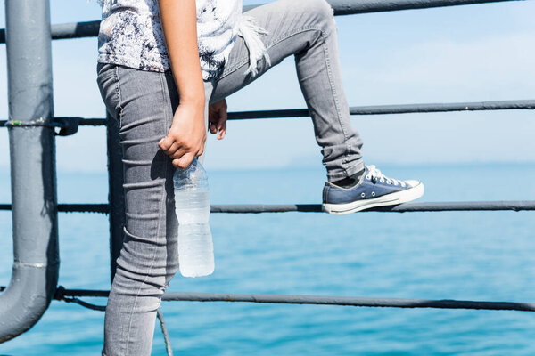 Teenager girl in unique stlye with trendy sneaker shoe holding bottle of cold water in sunny day