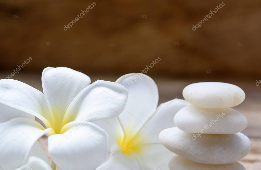 Pile of white zen stones and Frangipani flower on rustic wood background