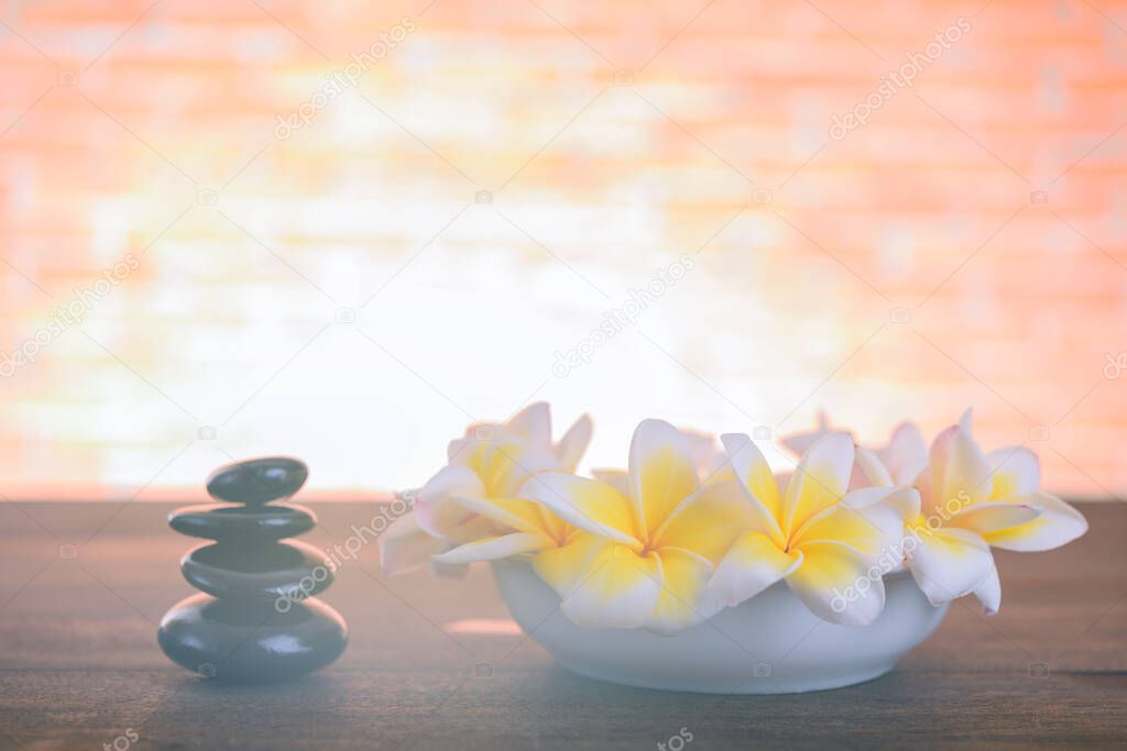 Beautiful Frangipani flowers in white bowl with black zen stones on wooden table with brick wall background