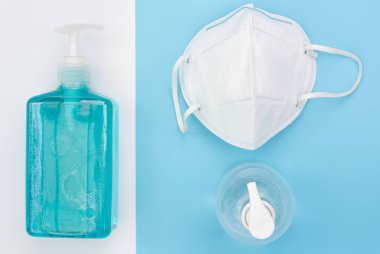 Mikrop koruması ve jel alkolü ya da el dezenfektanı şişesi takmak için cerrahi maske. Mavi ve beyaz arka planda bulunan Corona virüsünden korunmak için el yıkama spreyi şişesi.