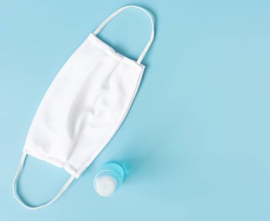 Mikrop koruması ve jel alkolü veya el dezenfektanı şişesi takmak için beyaz maske. Mavi arka plandaki Corona virüsünden korunmak için el yıkama spreyi.