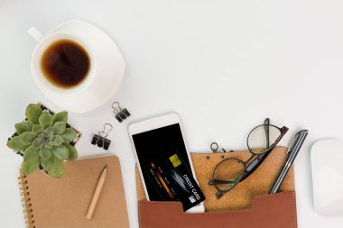 Çalışma alanı kompozitonu cep telefonu, kahve fincanı, defter, gözlük, kredi kartı ve yeşil yapraklar ile beyaz arka planda boşluk, üst görünümde