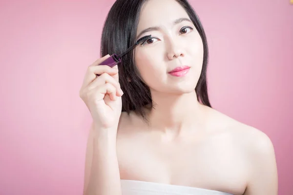 Длинные волосы азиатской молодой красивой женщины применяя тушь изолированы на розовом фоне. натуральный макияж, СПА-терапия, косметология, косметология и пластическая хирургия . — стоковое фото