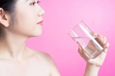 Sağlıklı Asyalı genç güzel kadın içme suyu, Güzellik yüz doğal makyaj, pembe bir arka plan üzerinde izole.