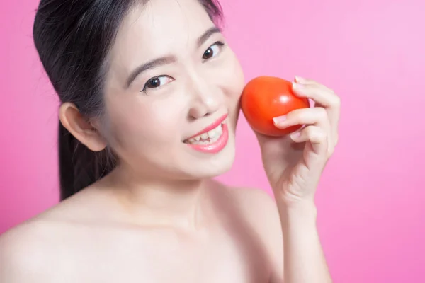 Азиатка с томатной концепцией. Она улыбается и держит помидор. Красота лица и натуральный макияж. Изолированный на розовом фоне . — стоковое фото
