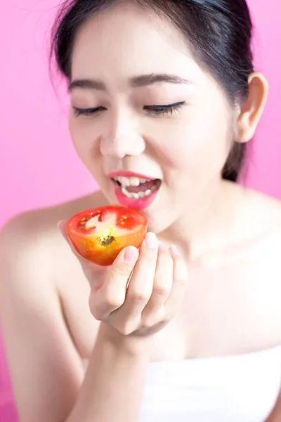 Azjatyckie kobiety z koncepcją pomidor. Ona uśmiecha się i przytrzymując pomidor. Piękna twarz i naturalny makijaż. Na białym tle różowy. — Zdjęcie stockowe