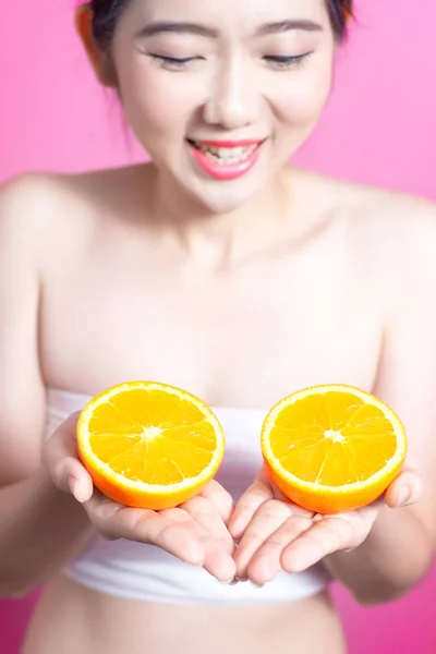 Mujer asiática con concepto naranja. Ella sonriendo y sosteniendo naranja. Cara de belleza y maquillaje natural. Aislado sobre fondo rosa . —  Fotos de Stock
