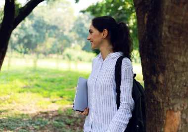 Güzel yaratıcı kadın gülümseme portresi ve kamu parkında çalışmak için dizüstü bilgisayar tutuyor..