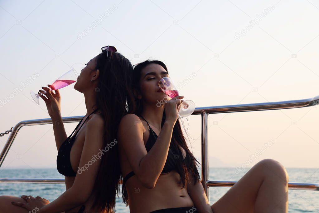 Beautiful Asia two young woman smile portrait traveling and drinking wine on speed boat in summer for relaxation at Thailand.
