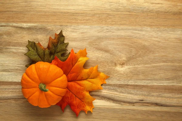 Pompoen en herfstbladeren op houten ondergrond — Stockfoto