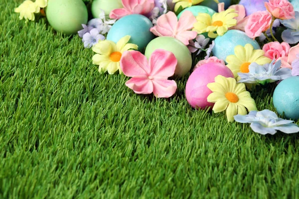 Telur Paskah berwarna di rumput dengan bunga latar belakang — Stok Foto