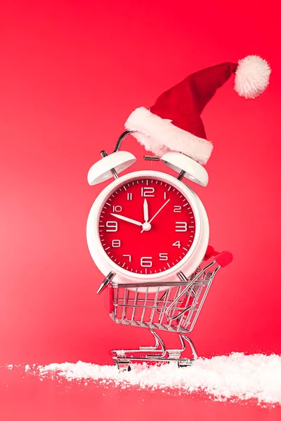 Sombrero de Navidad Santa en reloj rojo, equilibrado en el carrito de la compra. Las —  Fotos de Stock