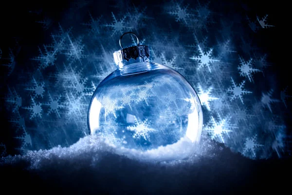Clear Christmas ornament in snow surrounded by a bokeh of glitte — Stock Photo, Image