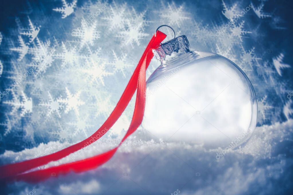 Clear Christmas ornament in snow surrounded by a bokeh of glitte