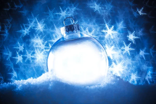 Adorno de Navidad claro en la nieve rodeado de un bokeh de brillo —  Fotos de Stock