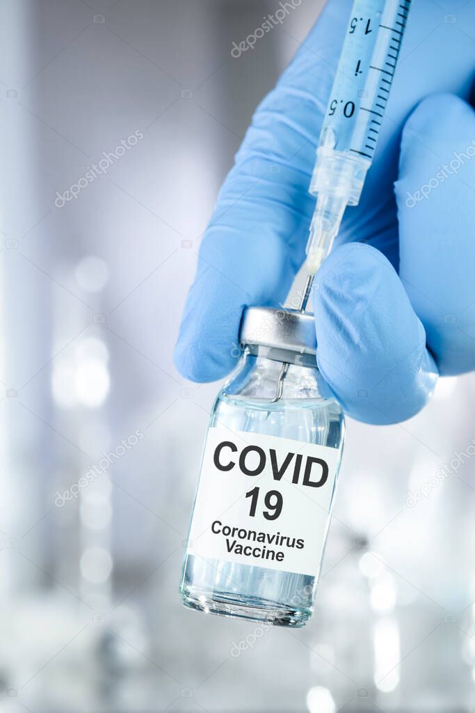 Healthcare cure concept with a hand in blue medical gloves holding Coronavirus, Covid 19 virus, vaccine vial