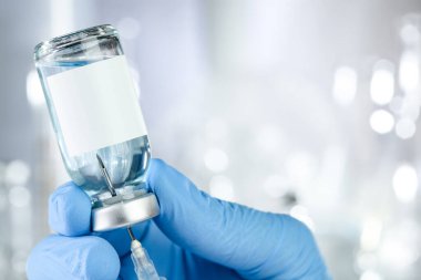 Mavi eldivenli bir el ile sağlık konsepti mavi sıvı ve siyah beyaz etiketli bir aşı şişesi tutuyor.