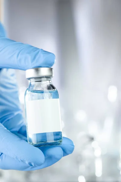 青い液体と黒の白いラベルのワクチン瓶を保持青い医療用手袋の手でヘルスケアの概念 — ストック写真