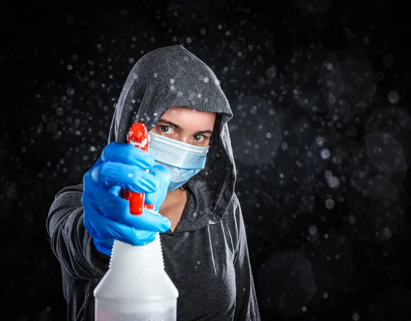 Woman wearing medical mask and cleaning gloves spraying a mist of disinfectant. Serious about keeping clean and virus free concept.