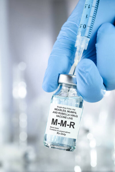 Healthcare concept with a hand in blue medical gloves holding MMR, measles mumps and rubella, vaccine vial and syringe needle