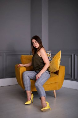 Kısa saçlı güzel bir kız sarı bir koltukta oturuyor.