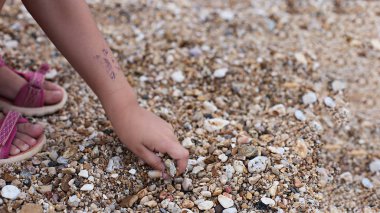 Deniz kıyısındaki kız kumla ve çakıl taşlarıyla oynar doğanın güzelliğini