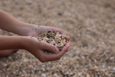 Deniz kıyısındaki kız kumla ve çakıl taşlarıyla oynar doğanın güzelliğini