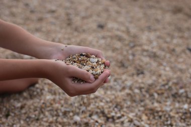 Deniz kıyısındaki kız kumla ve çakıl taşlarıyla oynar doğanın güzelliğini