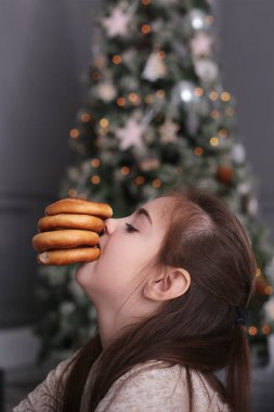 Uzun siyah saçlı güzel bir kız süslenmiş bir Noel ağacında yeni yıl ışıklarında kurabiyelerle oynaşıyor.