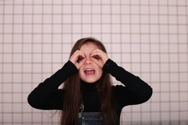 Sekiz yaşında, siyah balıkçı yakalı, uzun saçlı, siyah bir kafesin beyaz arka planında beyaz yakalı, farklı duyguları olan, gülümseyen genç bir kız.