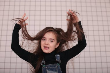 Sekiz yaşında, siyah balıkçı yakalı, uzun saçlı, siyah bir kafesin beyaz arka planında beyaz yakalı, farklı duyguları olan, gülümseyen genç bir kız.