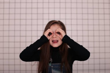 Sekiz yaşında, siyah balıkçı yakalı, uzun saçlı, siyah bir kafesin beyaz arka planında beyaz yakalı, farklı duyguları olan, gülümseyen genç bir kız.