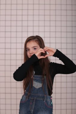 Sekiz yaşında, siyah balıkçı yakalı, uzun saçlı, siyah bir kafesin beyaz arka planında beyaz yakalı, farklı duyguları olan, gülümseyen genç bir kız.