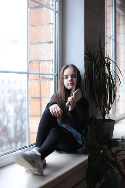 young kind playful girl of eight years with long hair in a black turtleneck and denim sundress with the sign \