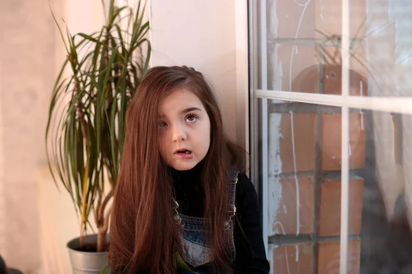 young kind playful girl of eight years with long hair in a black turtleneck and denim sundress with the sign \