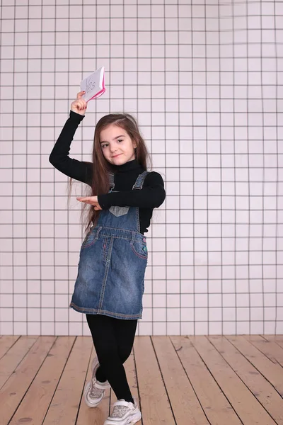 young kind playful girl of eight years with long hair in a black turtleneck and denim sundress with the sign \